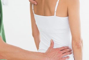 Rear view of a male physiotherapist examining woman's back in the medical office