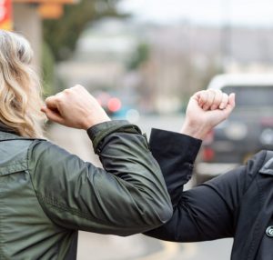 Elbow bump. New greeting to avoid the spread of coronavirus. Two women friends meet in British street with bare hands. Instead of greeting with a hug or handshake, they bump elbows instead. Vertical.